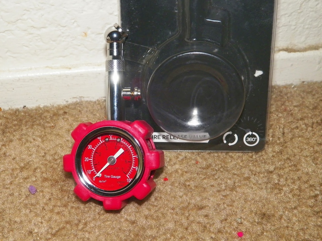 Närbild på en röd analog däcktrycksmätare med tryckskala från 0-100 psi.